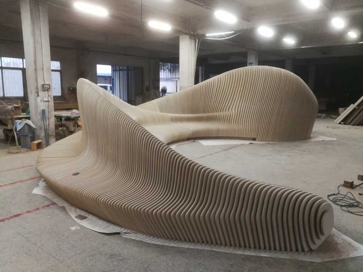 Sleek and modern furniture piece featuring a sculptural wooden form with a flowing design, being handcrafted in a production environment.