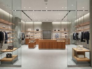 A sleek, minimalist retail store, featuring clean lines, frameless glass displays, and soft integrated lighting. The space is open and uncluttered, with strategically placed high-end products that draw attention. A combination of metal, glass, and wood elements adds texture, ensuring a refined yet inviting atmosphere. The overall ambiance is modern, luxurious, and intentionally designed to enhance the shopping experience.