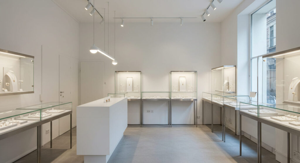 A modern small jewelry boutique interior, minimalistic Bauhaus-inspired design, clean white walls, polished floor, elegant jewelry showcases with subtle lighting, focus on atmosphere and layout.